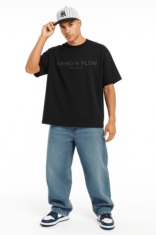 Men's oversize streetwear t-shirt by Grind n Flow in black, paired with wide-leg jeans and sneakers, featuring bold 3D front logo.
