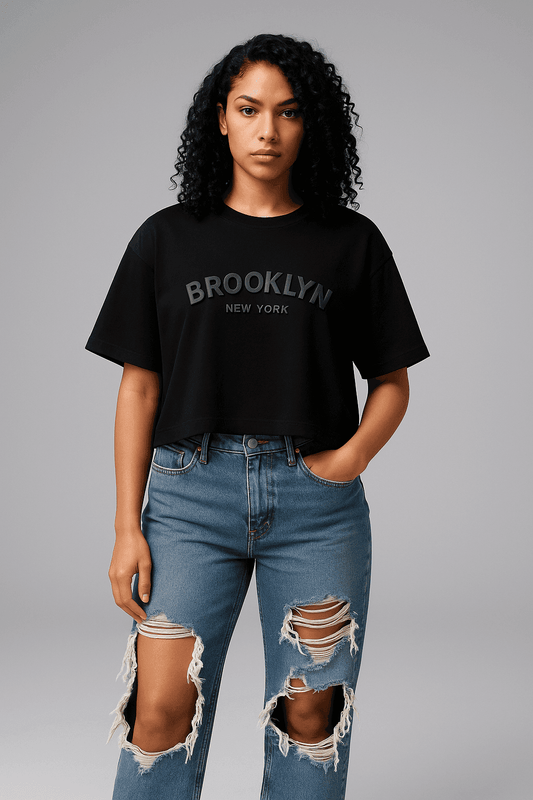 Brooklyn Crop Top - Women's Crop Tee in black with bold 'Brooklyn New York' text, styled with ripped jeans for a casual streetwear look.