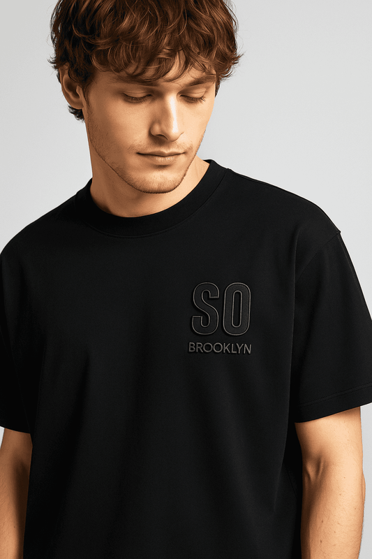 Close-up of men's black oversize t-shirt featuring 3D 'SO BROOKLYN' chest logo. Streetwear design crafted from soft organic cotton.