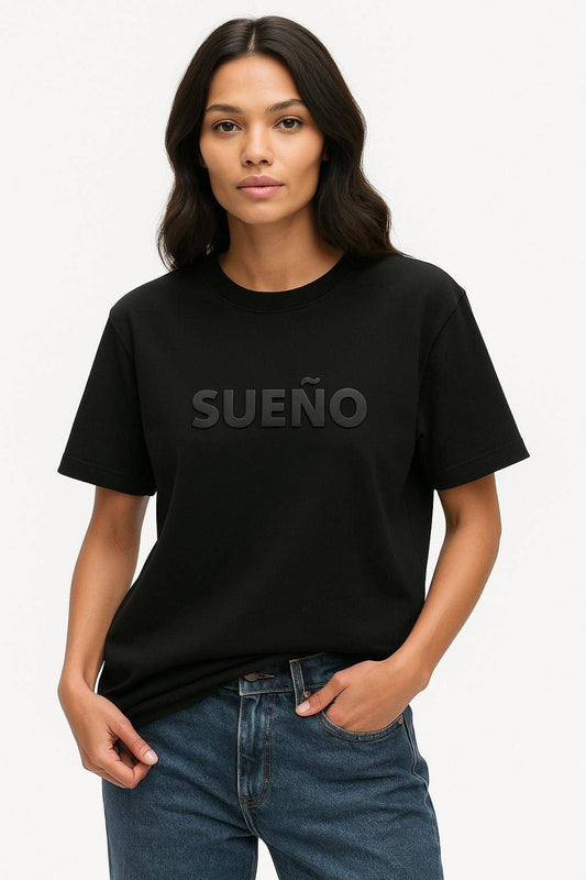 Black Sueno - Dream Spanish Tee featuring bold 3D 'SUEÑO' text, modeled by woman in casual jeans. Ideal Latina motivation shirt gift.