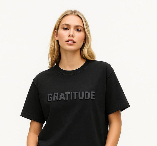 Close-up of Gratitude Women’s T-Shirt featuring 3D 'GRATITUDE' text on soft black cotton. Inspirational and minimalist graphic tee.