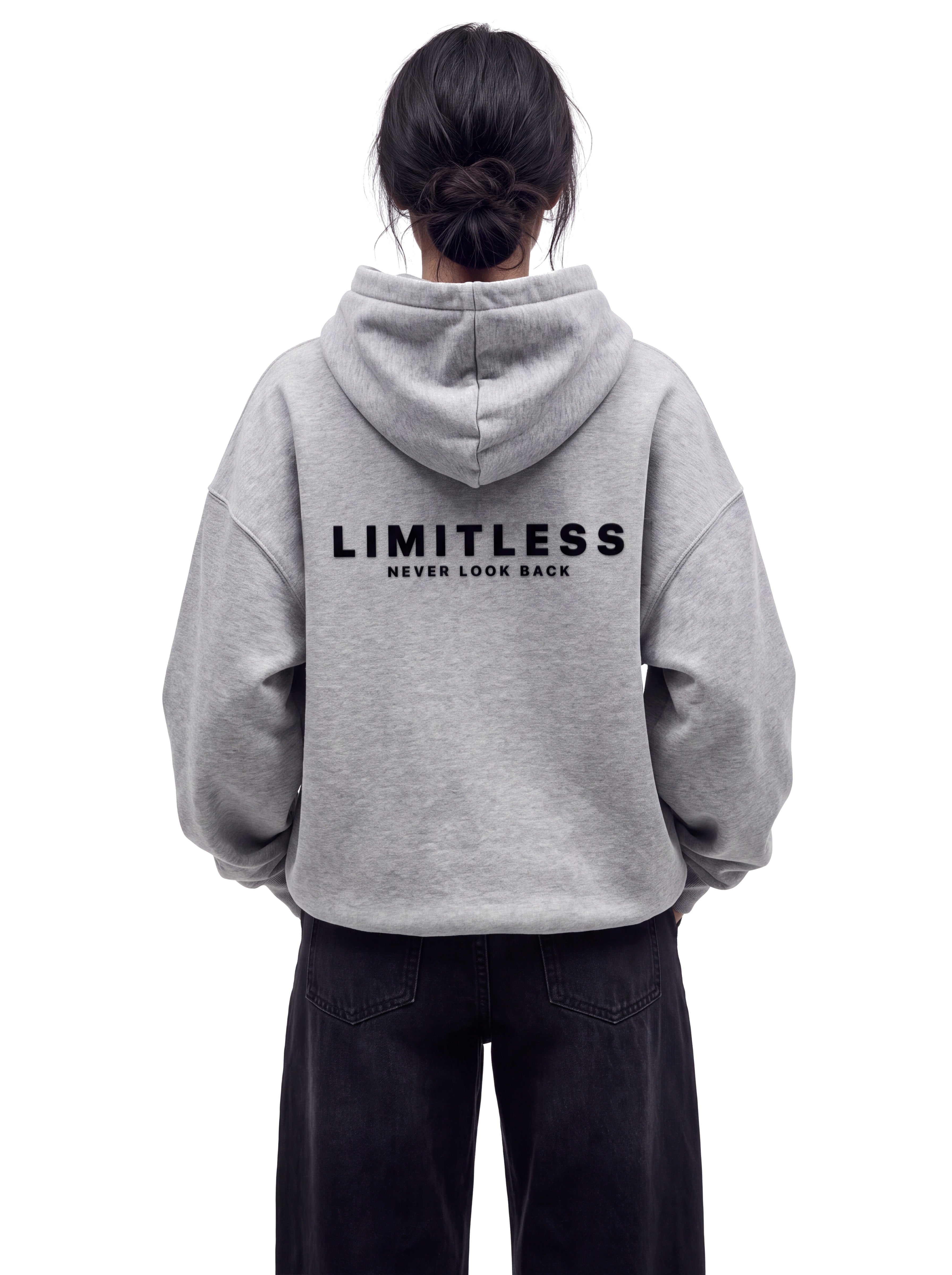 Back view of woman in super oversized heather grey LIMITLESS fleece hoodie, both hands in the front pocket, showing raised flock LIMITLESS / NEVER LOOK BACK back print